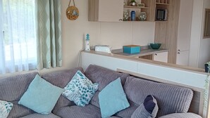 Un área de estar moderna con un sofá seccional, una cocina con armarios de madera y un accesorio de luz en el techo.
