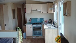 Cocina compacta con estufa, horno y pileta. Un pequeño comedor incluye un sofá y una planta en maceta.