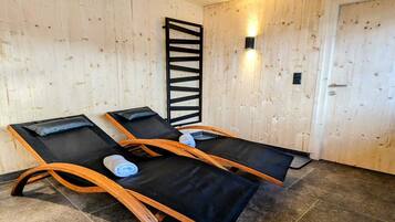 Relax in a serene sauna with three loungers, a bathtub, and a wall-mounted light fixture.