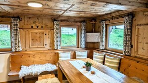 A wooden cabin interior with a wooden bench, a dining table with a placemat, and a view of greenery outside through the windows. - Spacious Holiday Home in Distelberg With Sauna (Aschau Im Zillertal)