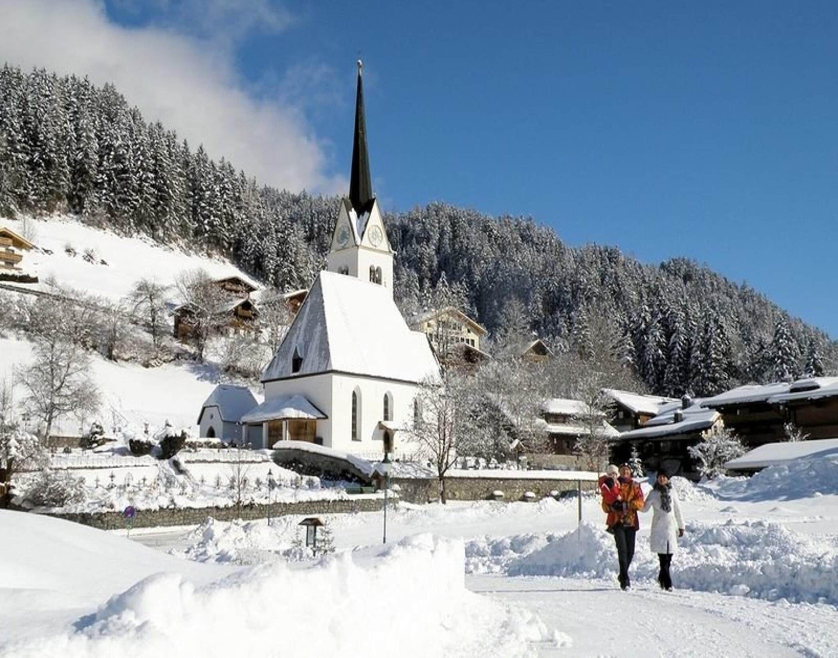 A snow-covered village with a prominent church, traditional buildings, and a clear blue sky.