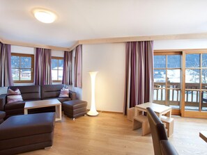 A modern living room with a sofa, ottoman, and coffee table, large windows with curtains, and a view of a snowy landscape.