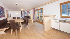 A modern kitchen with wooden cabinets and a dishwasher, a dining area with a wooden table and chairs, and large windows with curtains. - Apartment in Wald im Pinzgau Near the ski Lifts (Wald im Pinzgau)