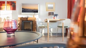 A modern living room with a glass coffee table, a flat-screen TV mounted on the wall, and a dining area with a wooden table and chairs. - Small Studio in Neuastenberg With Balcony (Winterberg)