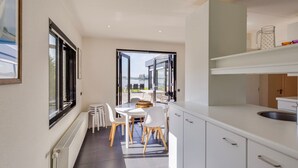 A modern kitchen with white cabinets, a dining area with a table and chairs, and a view of the outdoors through large windows. - Lakeside Stay in Kamperland (Kamperland)