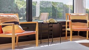A modern room with two wooden chairs and a small table, large windows with a view of greenery, and a black-framed picture frame on the table. - Lakeside Stay in Kamperland (Kamperland)