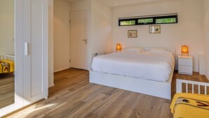 A bedroom with a large bed, a white wardrobe, a wooden floor, and a window with blinds. - Lakeside Stay in Kamperland (Kamperland)