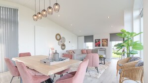 A modern living room with a wooden dining table, pink chairs, a grey sofa, and a large plant. - House in Zeeland With Terrace by the Dyke (Wemeldinge)