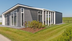 A modern building with a sloped roof, large windows, and a covered outdoor area. - House in Zeeland With Terrace by the Dyke (Wemeldinge)