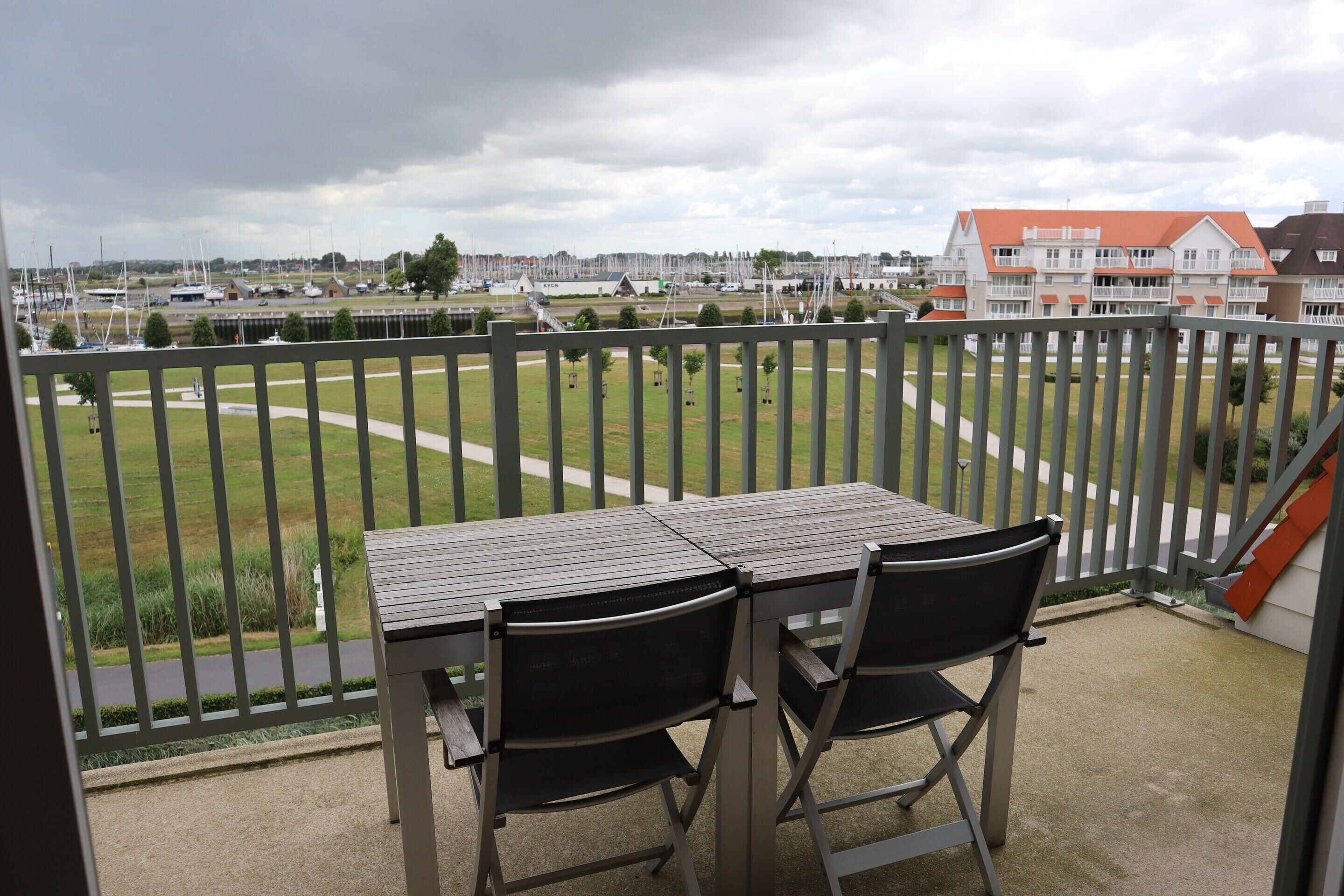 Ein Balkon mit Tisch und Stühlen, Blick auf einen Yachthafen mit Booten und einer Rasenfläche.