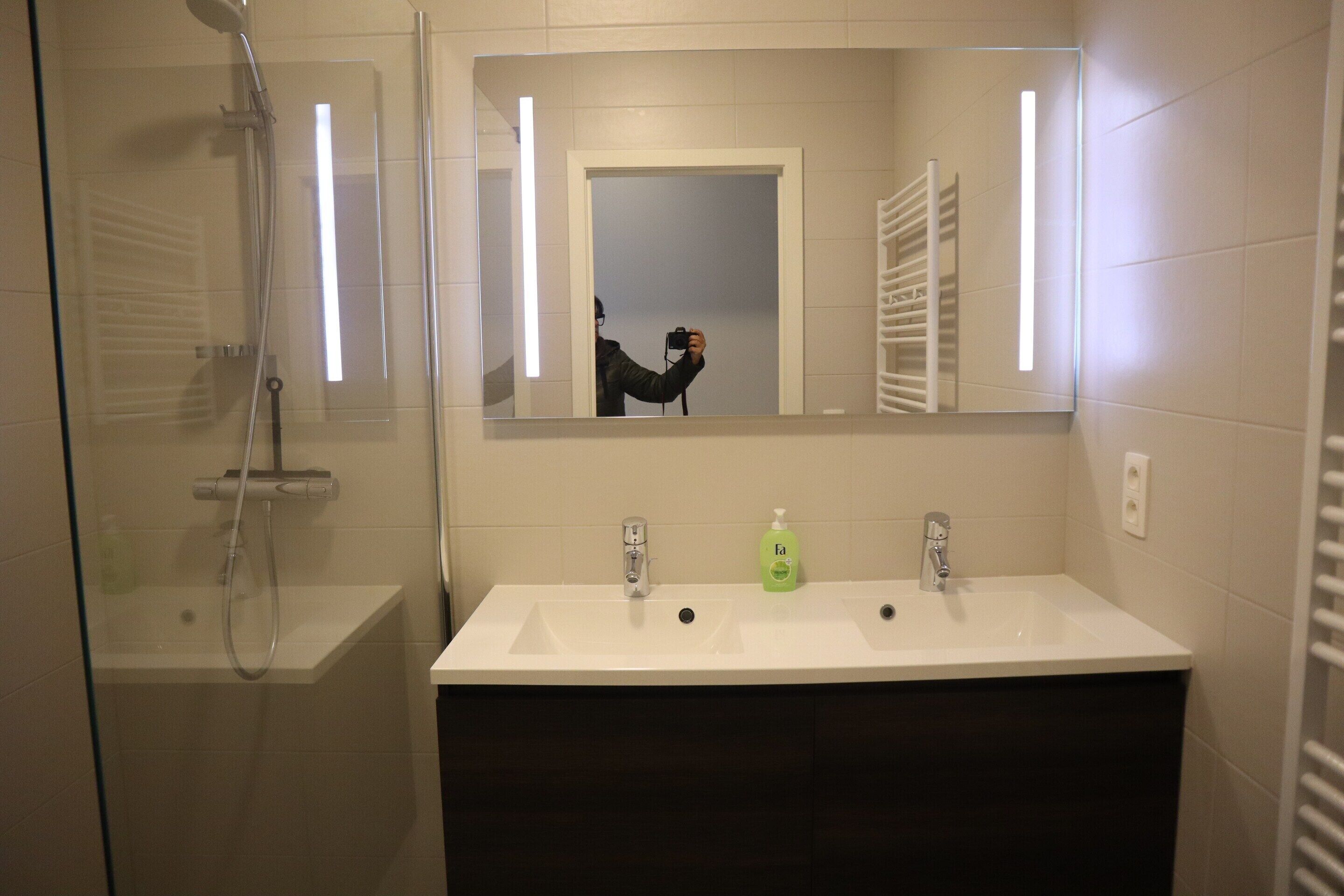 Un baño con ducha, dos lavamanos y un espejo.