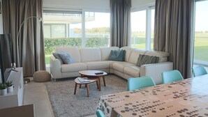 A modern living room with a sectional sofa, a round coffee table, and a dining table with a patterned tablecloth. - Apartment in Nieuwpoort Near the Marina (Nieuwpoort)