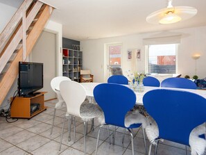 A dining area with a white table, blue chairs, and a television on a wooden stand.