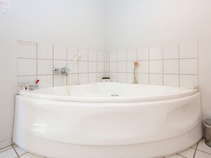 A large, empty bathtub in a bathroom with white tiled walls and a small trash bin to the right.