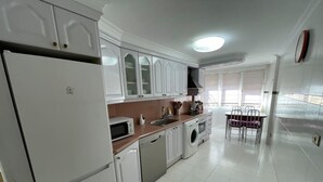 A modern kitchen with white cabinets, a microwave, a washing machine, and a dining area with a table and chairs. - Bermeo Park - Centrica Casa Independiente (Bermeo)