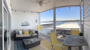 En balkon med en sofa, et bord og stole, med udsigt over vand og en bro.
