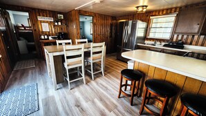 Un acogedor interior de cabaña con una zona de comedor de madera, una cocina con refrigerador y una barra con taburetes.