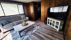 A living room with a sofa, coffee table, TV stand, and wooden flooring. - Cozy cabin on Little McDonald with amazing walk out beach! (Perham)