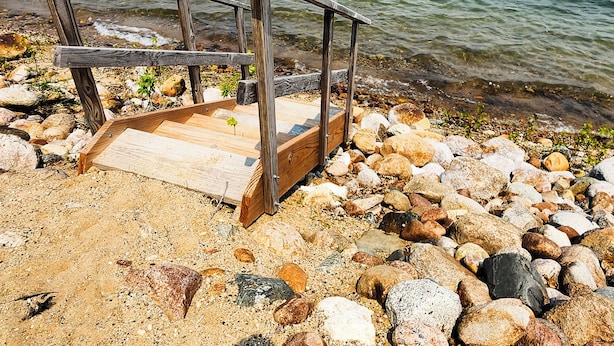 Un muelle de madera que se adentra en una masa de agua, rodeado de una costa rocosa.