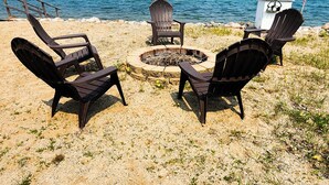 Escena de playa con tres sillas Adirondack dispuestas alrededor de un brasero circular.