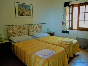 A room with two beds, floral headboards, a painting on the wall, a window with curtains, and a radiator. - Holiday Home Casa Solaria (Sinnai)
