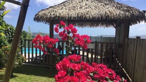 A thatched-roof structure with a pool in the background. - Saphir et sa Piscine à Débordement 3D Avec Bar à Punch Intégré (Saint-Joseph (Martinique))