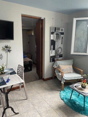 A living room with a dining area, a sofa, a TV, and a large window.