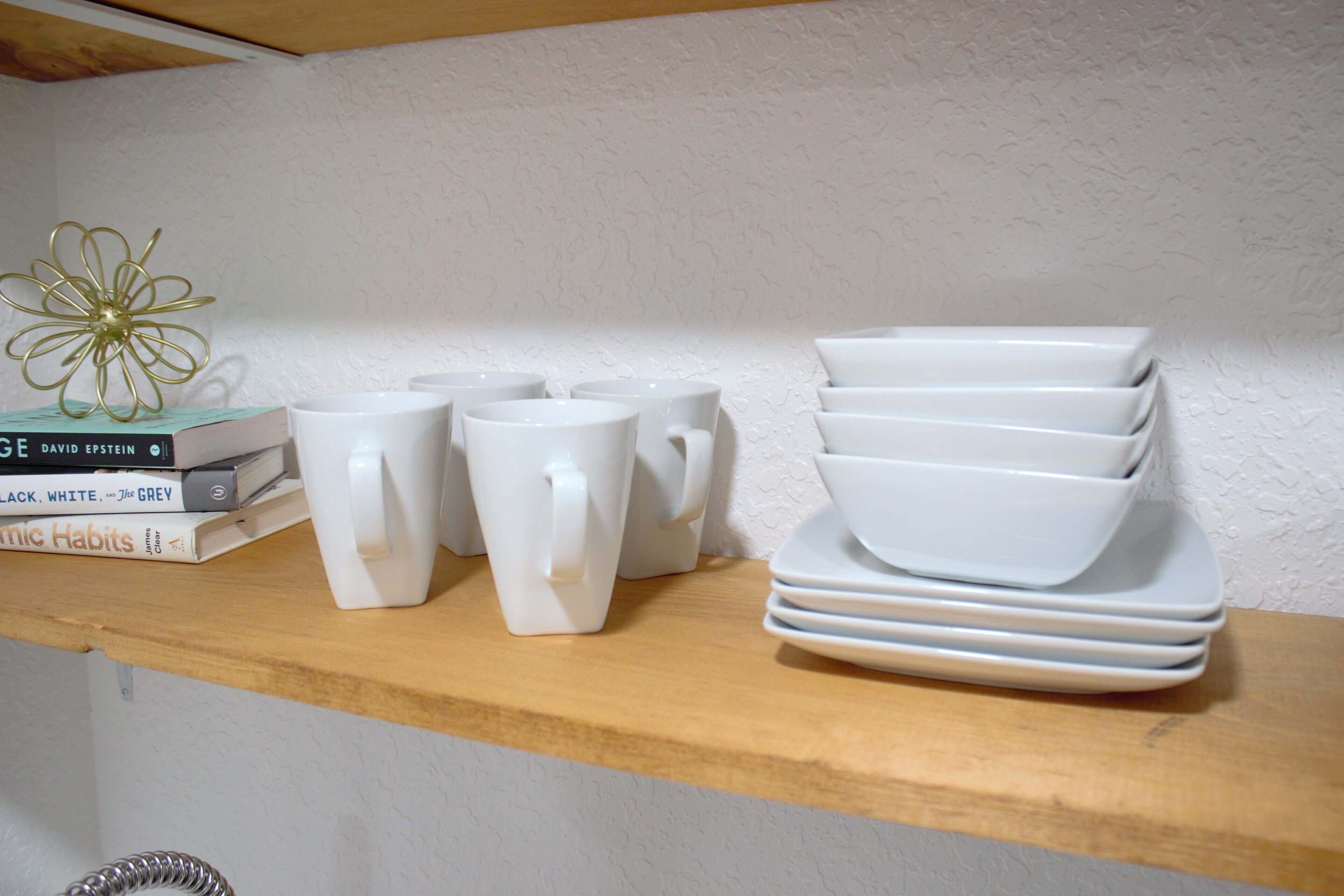 Une étagère avec des tasses, des assiettes et des livres, le tout de couleur blanche.