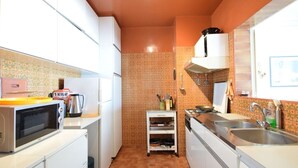 Een compacte keuken met witte kastjes, een magnetron, een waterkoker en een klein plankje met keukengerei.