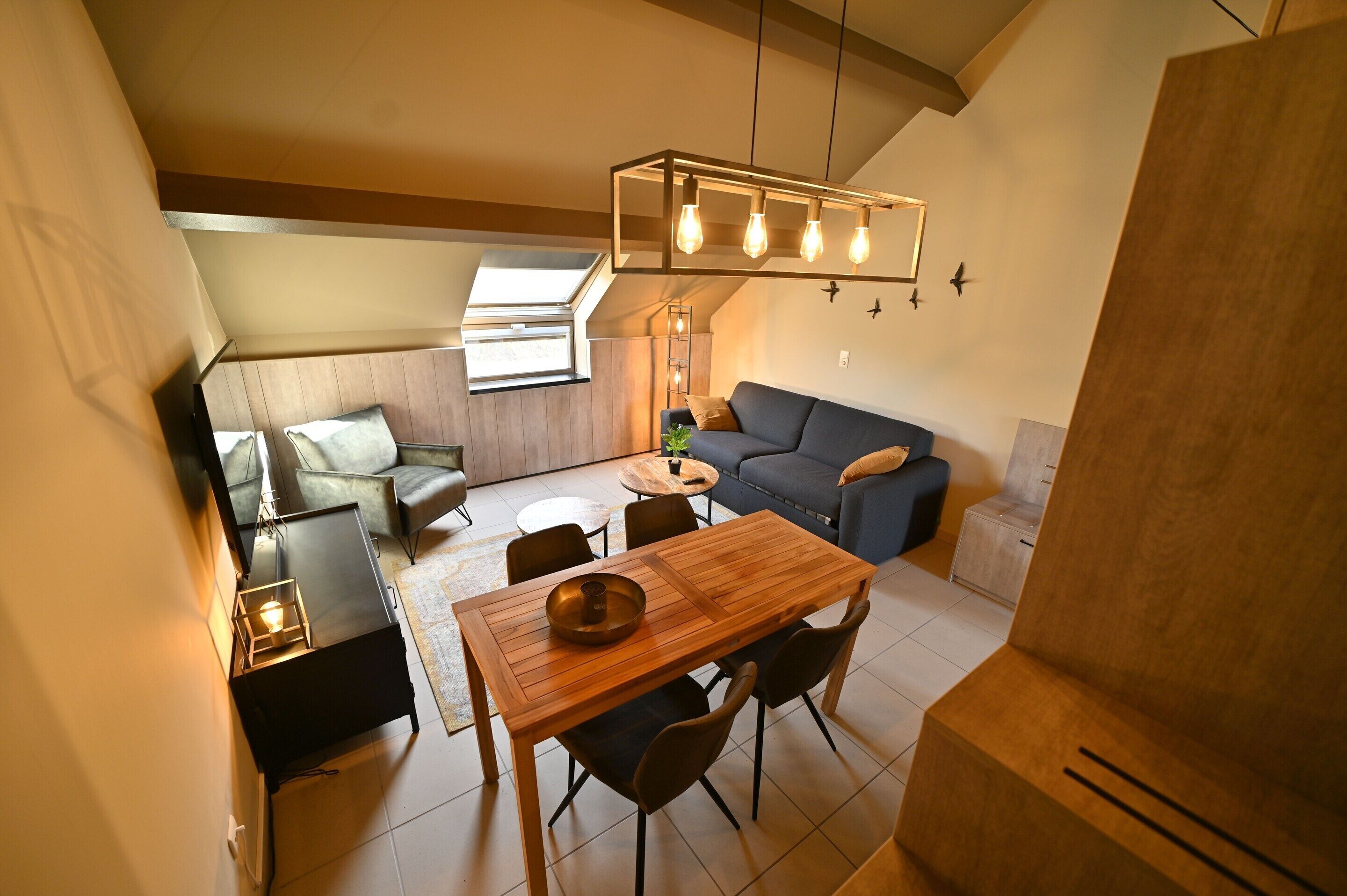 A cozy living area with a wooden dining table, blue sofa, and a hanging light fixture.
