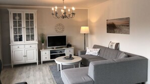 A modern living room with a grey sofa, a flat-screen TV, a cabinet, a chandelier, and a painting on the wall. - Huus Schippe "stockholm" (Maasholm)