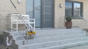 A building with a grey door labeled "Haus Schippe," a set of stairs with a metal railing, and a potted plant on the landing. - Huus Schippe "stockholm" (Maasholm)