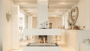 Un intérieur moderne avec une cheminée centrale, des meubles blancs et un élément décoratif mural.