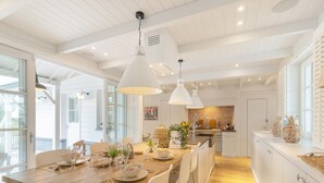 Une cuisine moderne avec des meubles blancs, un îlot central en bois, des luminaires suspendus et une vue sur la salle à manger.