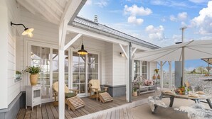 Une terrasse extérieure couverte, aménagée avec du mobilier en bois, une table dressée pour le repas et un grand parasol.