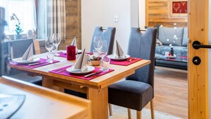Un comedor con una mesa de madera dispuesta para dos personas, dos sillas grises, una vela roja y un reloj en la pared.