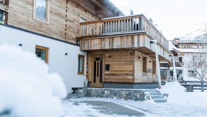Una cabaña de madera con balcón, escalones de piedra y suelo cubierto de nieve.