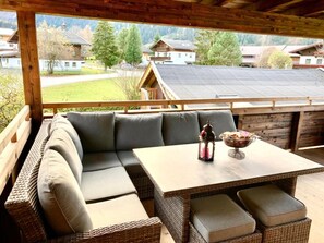 Un espace extérieur aménagé, abrité et doté d'un canapé et d'une table en osier, offrant une vue sur un quartier résidentiel avec ses maisons et ses arbres.