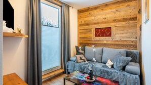 Una sala de estar acogedora con un muro de madera, un sofá gris y una mesa de centro colorida.
