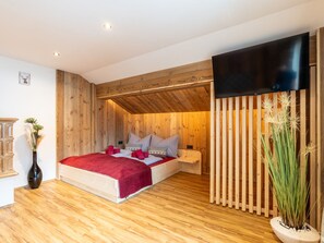 Une chambre confortable avec un plafond en bois, un lit avec une literie rouge, un téléviseur à écran plat et une plante en pot.