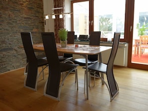 Comedor con mesa de madera, cuatro sillas, una planta en maceta y vistas al exterior a través de amplios ventanales.