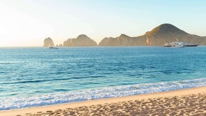 A beach with clear water, a sandy shore, and a yacht in the distance. - Best Resort in Cabo, Right on Medano Beach, Wonderful Staff, Gourmet Dining, spa (Cabo San Lucas)