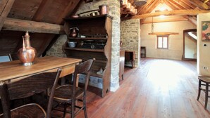 Interior rústico de madeira com parede de pedra, vigas de madeira, uma mesa e cadeiras de madeira.