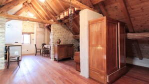Quarto rústico com vigas de madeira, parede de pedra, um armário de madeira e um espaço de jantar com cadeiras e mesa.