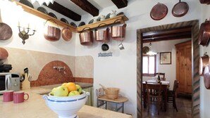 Uma cozinha com bancada de mármore, uma tigela de frutas e utensílios de cobre pendurados na parede.