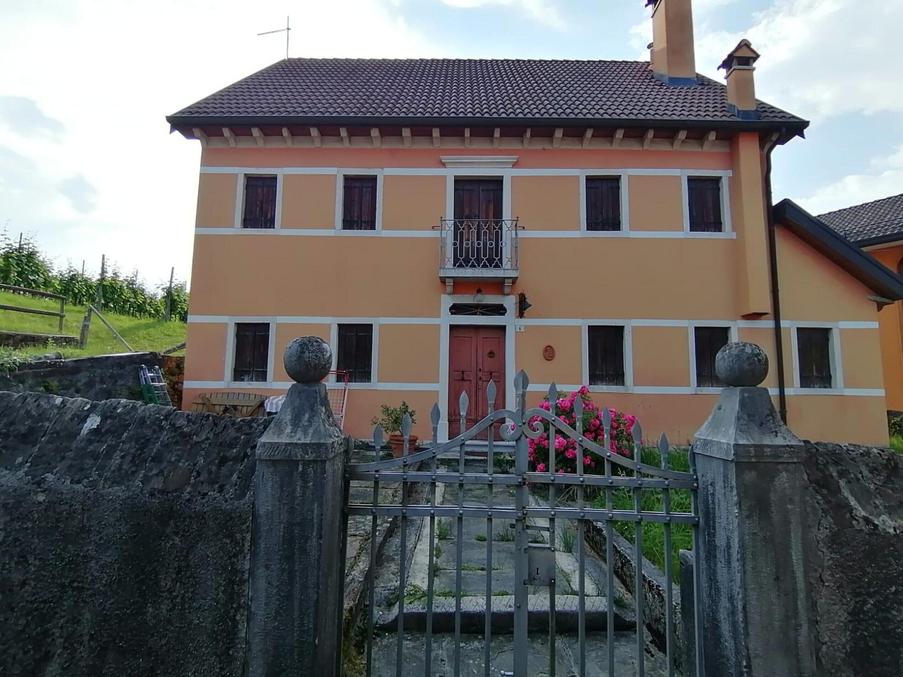 A two-story house with a balcony, a red door, and a metal gate.