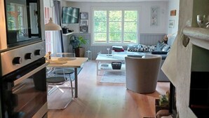 Cozinha moderna com forno embutido e micro-ondas, área de jantar com mesa e cadeiras, e sala de estar com sofá e uma janela grande.