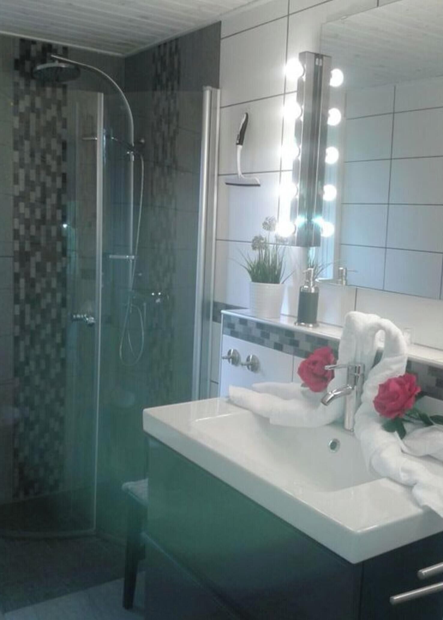 A modern bathroom with a glass-enclosed shower, a vanity with two sinks, and a mirror with lights.