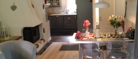 A modern living room with a fireplace, a dining area with a table and chairs, and a kitchen in the background.