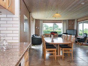 A spacious dining area with a wooden table and chairs, a sofa, and a television. - 4 Star Holiday Home in Glesborg (Glesborg)